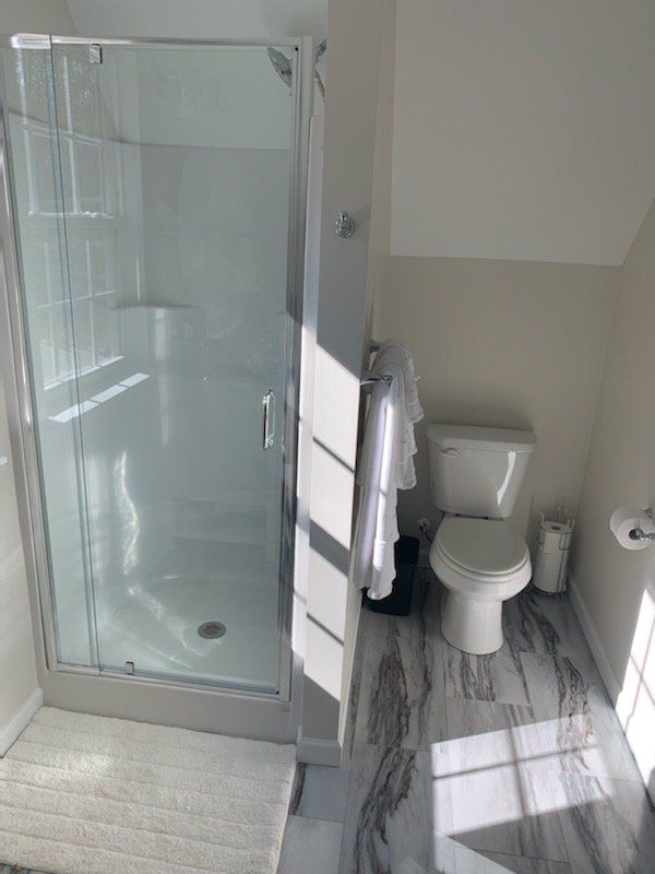 Bathroom with glass shower, white toilet, and gray marble-look floor.