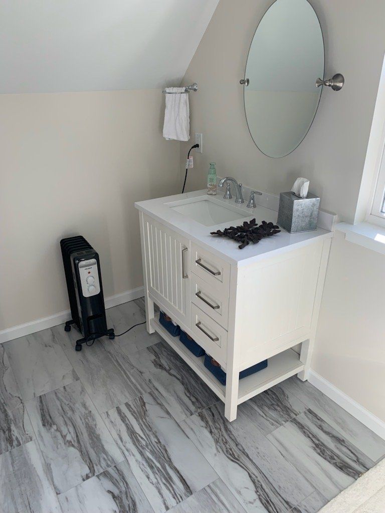 Bathroom with white vanity, oval mirror, gray floor, towel rack, and a space heater.