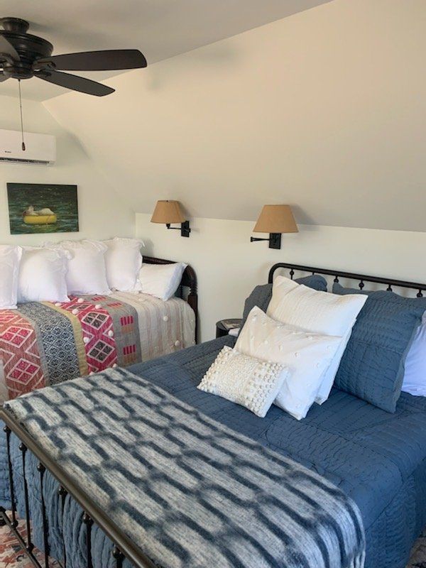 Bedroom with two beds, one with blue bedding, the other with a patterned blanket. Wall sconces and artwork are present.