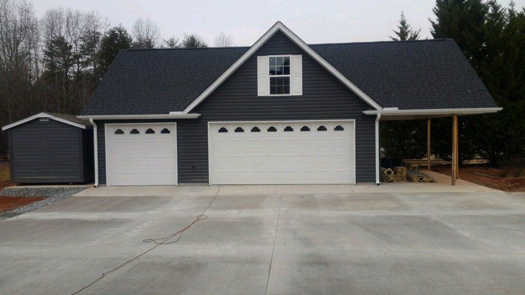 A gray garage with two white doors, a shed, and an attached carport.