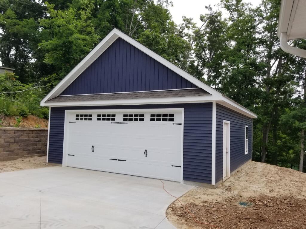 Blue and white garage with a concrete driveway, set against a backdrop of trees.