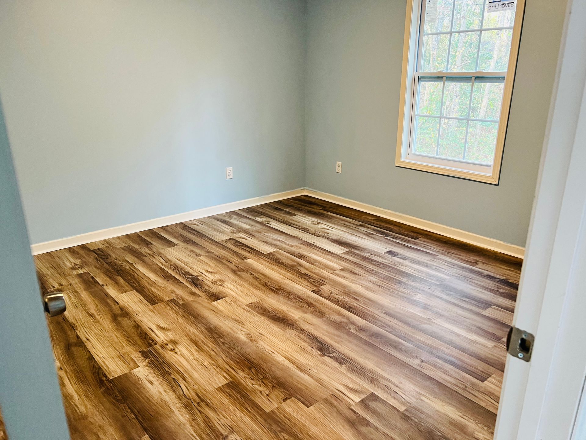 Empty room with wood-look flooring, light blue walls, and a window.