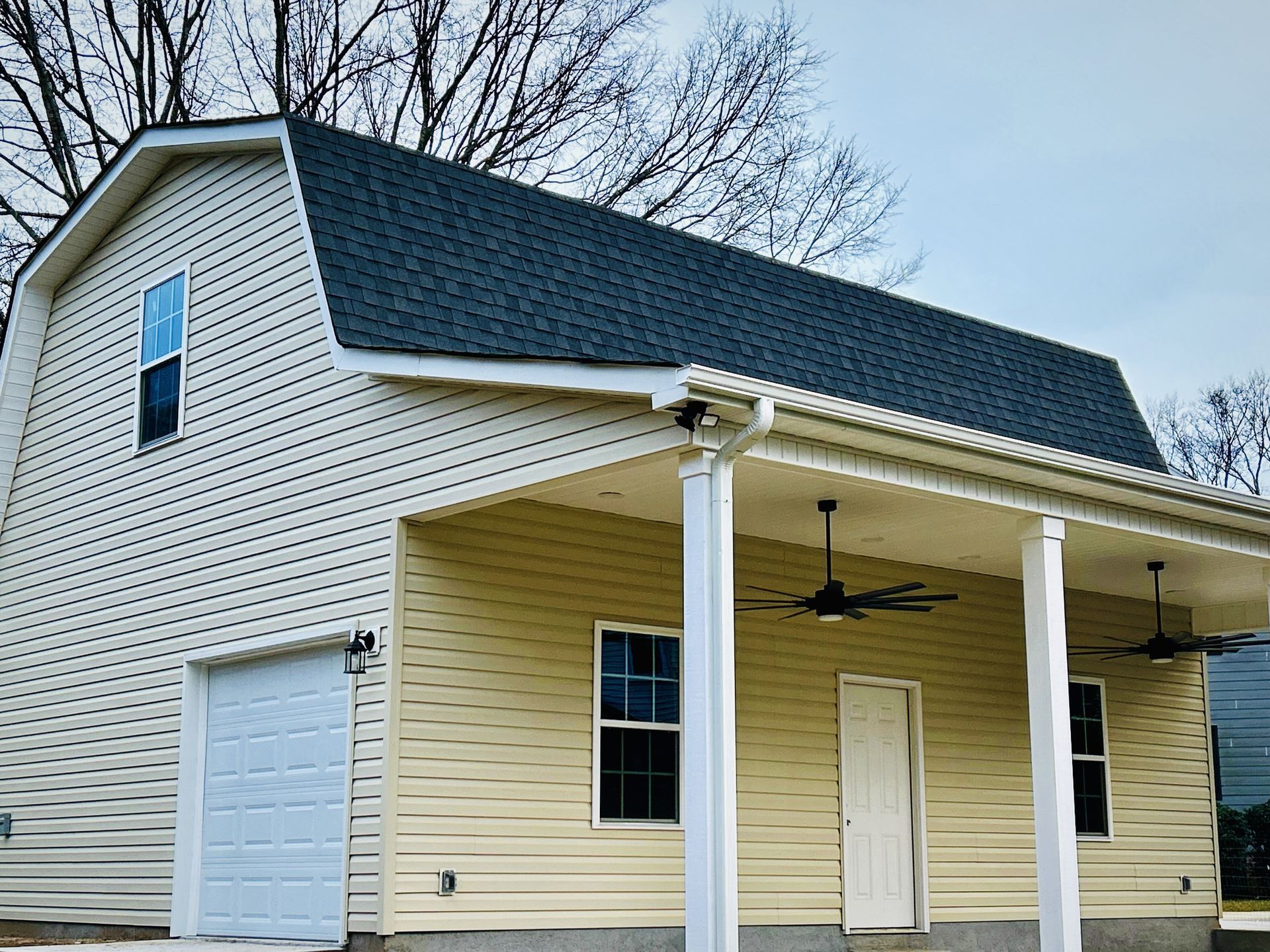 Two-story building with a garage and covered porch; tan siding, dark roof, blue sky.