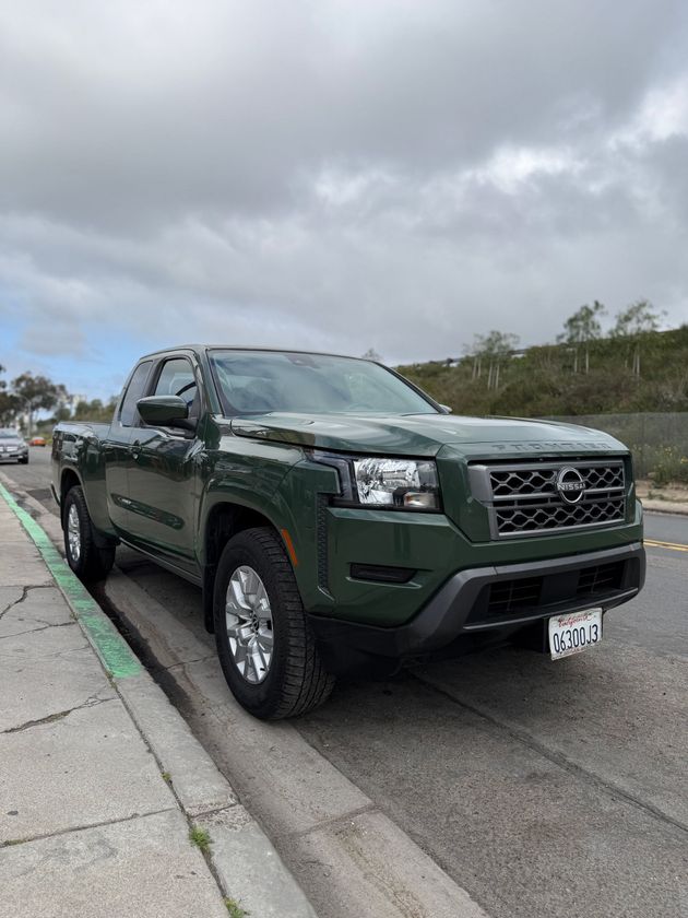 Dark green pickup truck parked by a curb under a cloudy sky