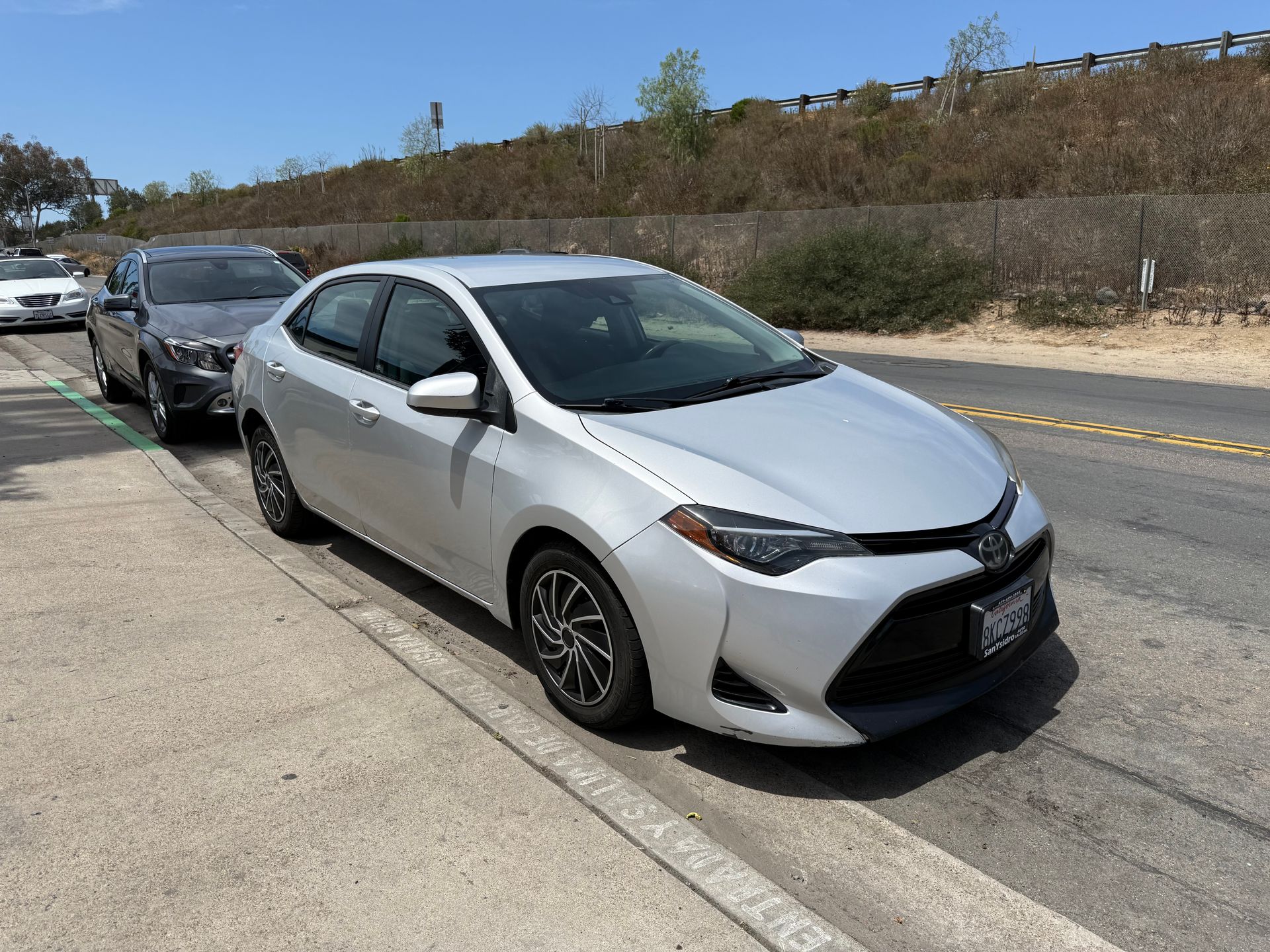 Silver sedan parked on a curb beside another car along a roadside under a clear sky
