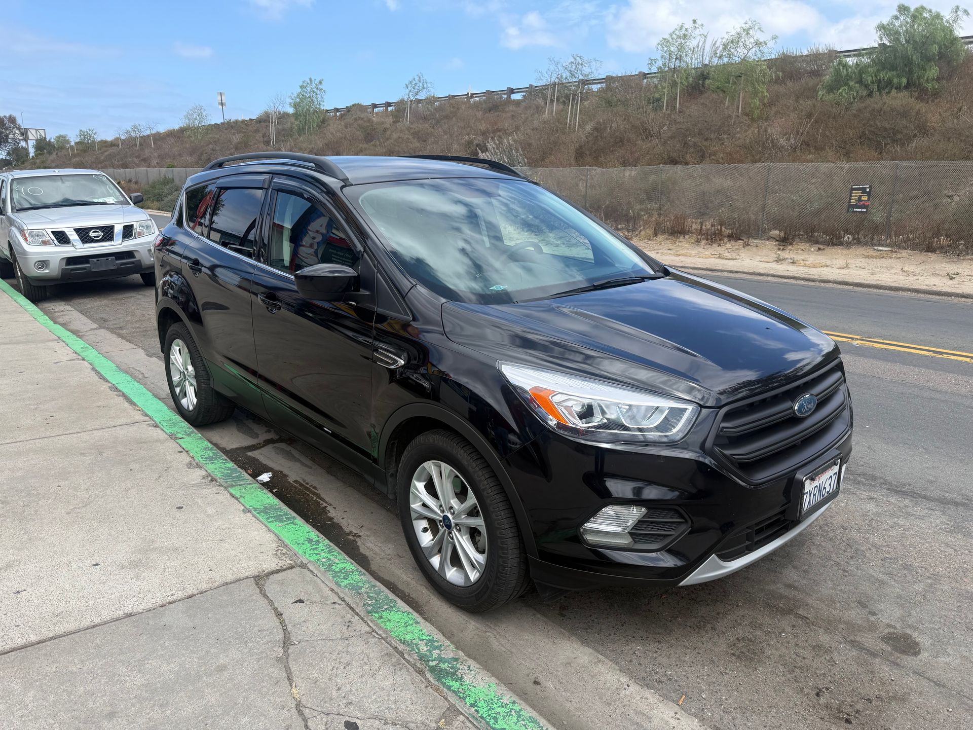 Black SUV parked on a roadside with another white car behind it under a cloudy sky
