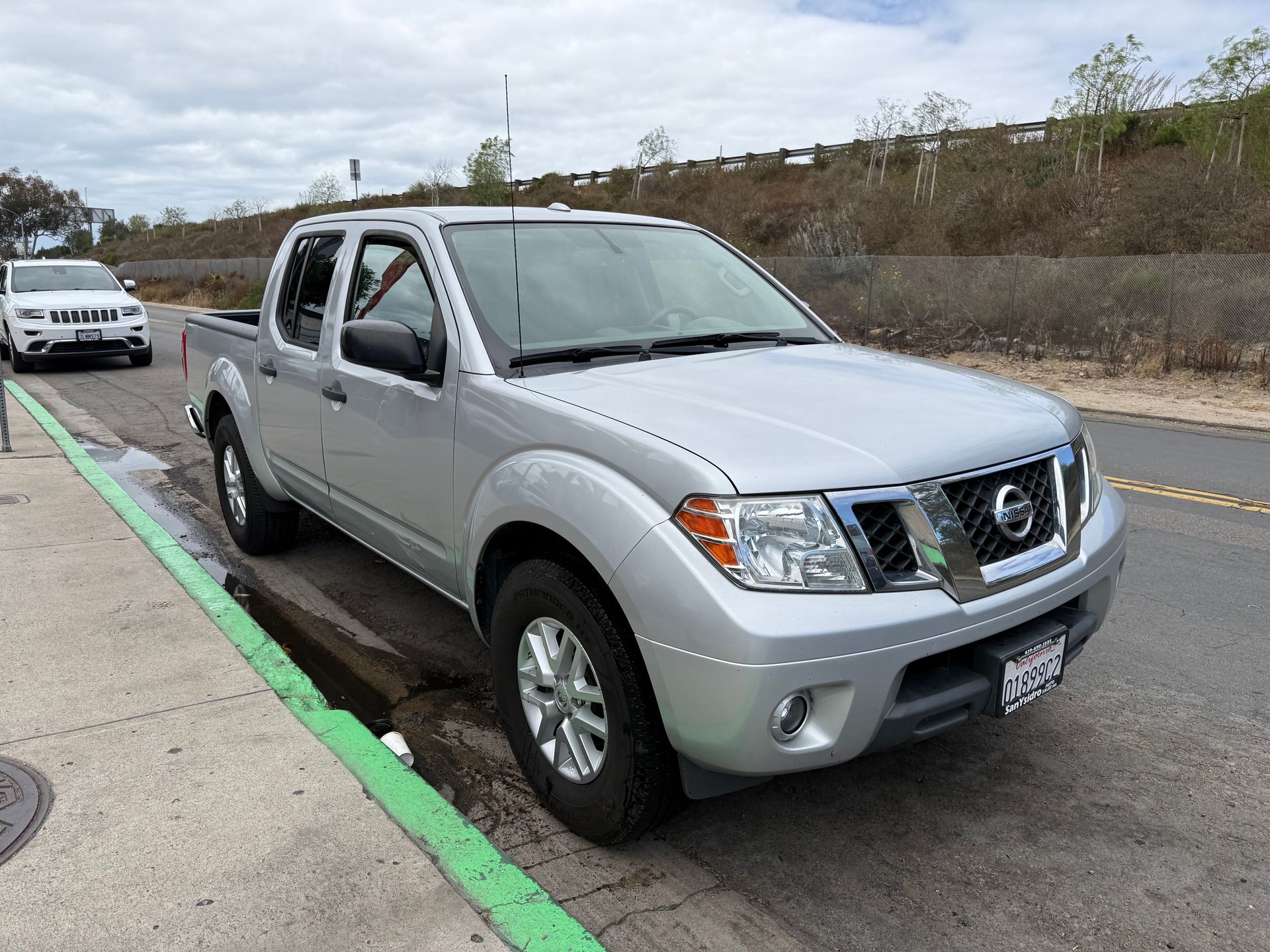 Silver Nissan pickup truck parked along a curb on a roadside.