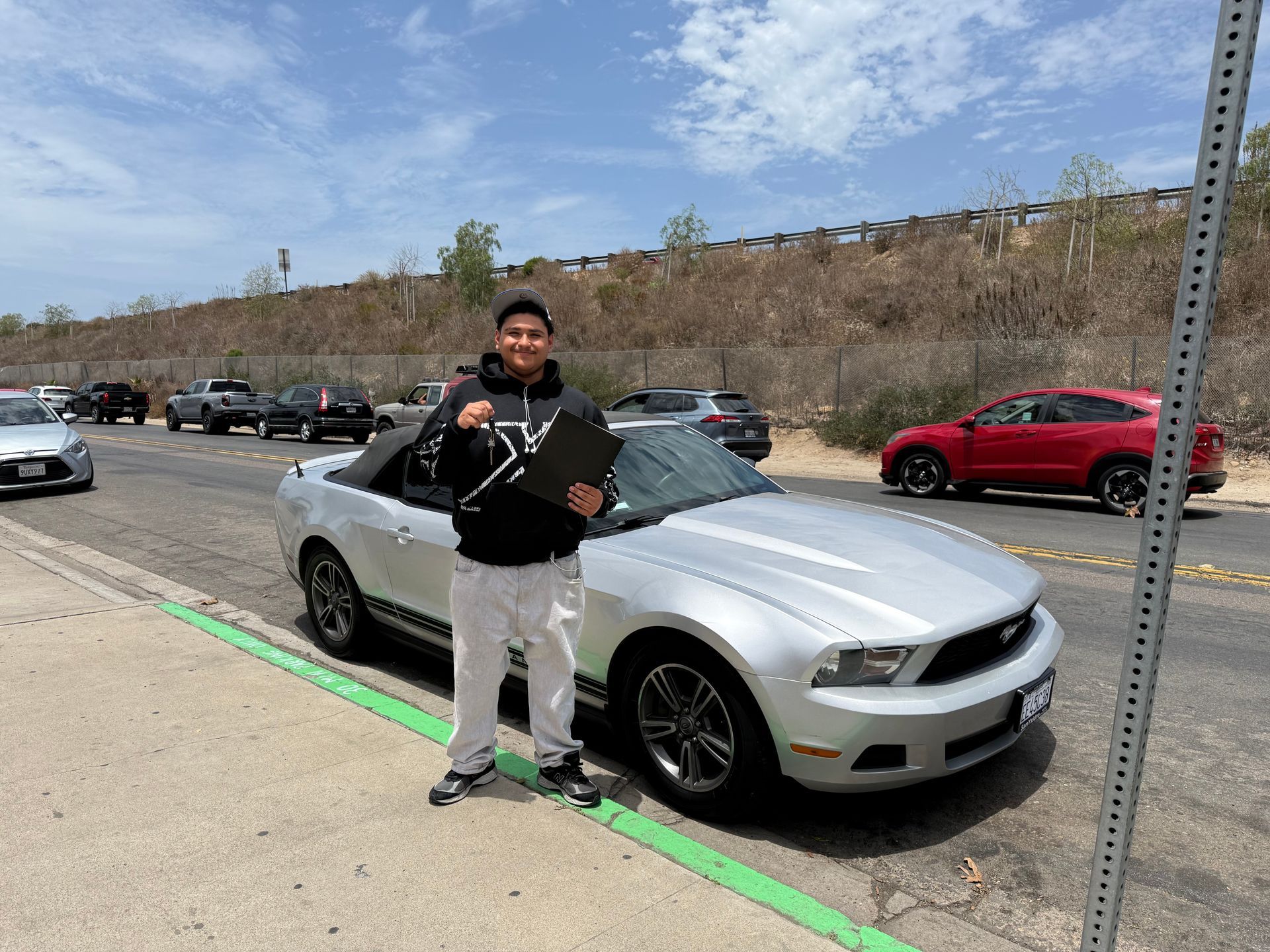 Person standing beside a silver sports car in a parking lot, holding a trophy.
