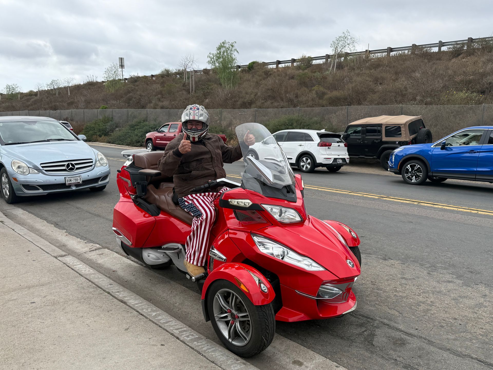 Person riding a red three-wheeled motorcycle on a road with traffic.