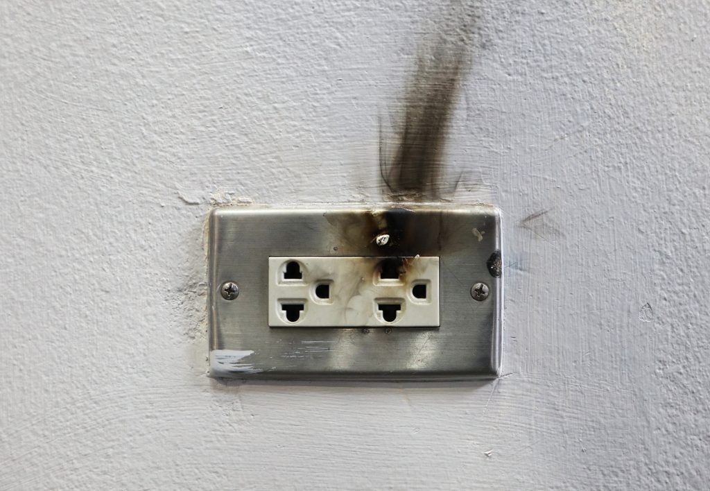 A broken electrical outlet on a wall with smoke coming out of it.