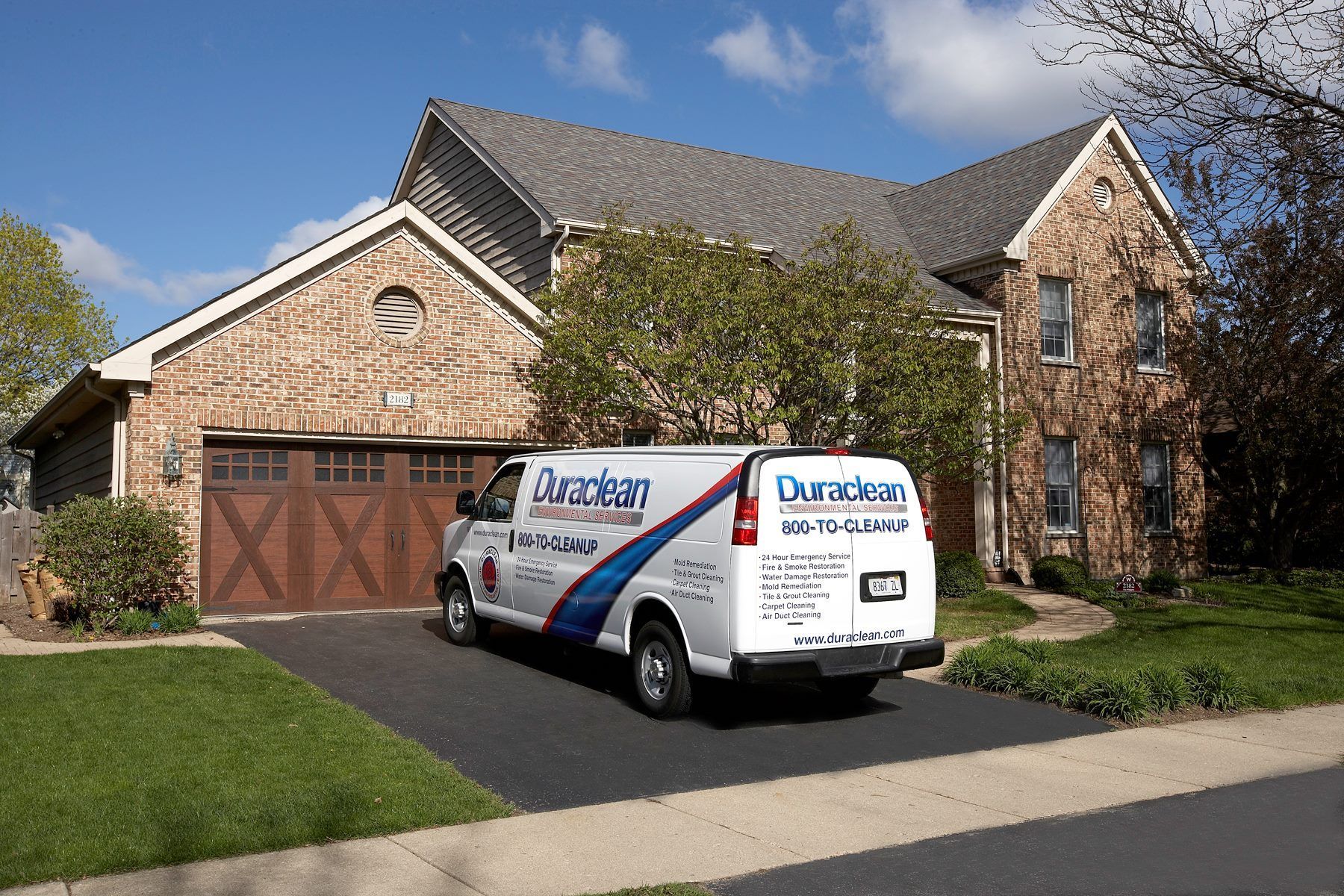 A blue and white van is parked in front of a brick house.