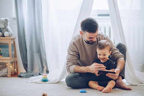 A father and son are sitting on the floor playing with a tablet.