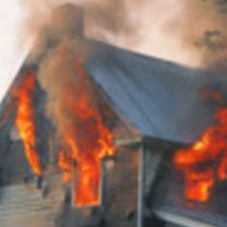 A house with flames and smoke coming out of the windows and roof.
