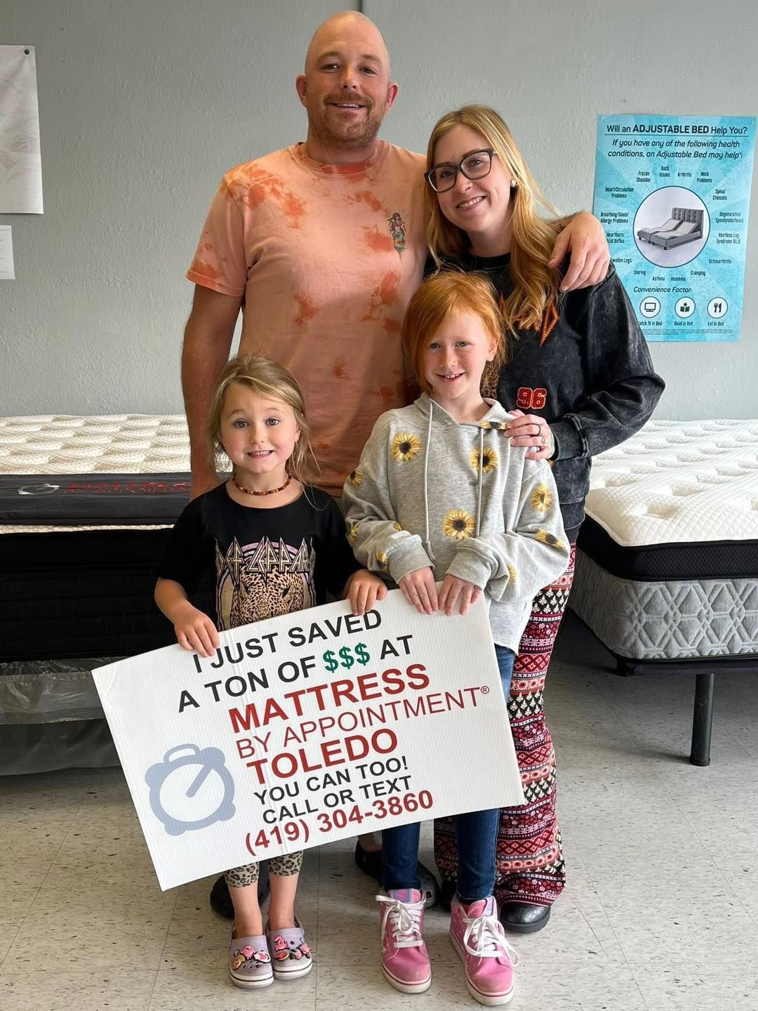 Family of four in a mattress store, holding a sign that reads,