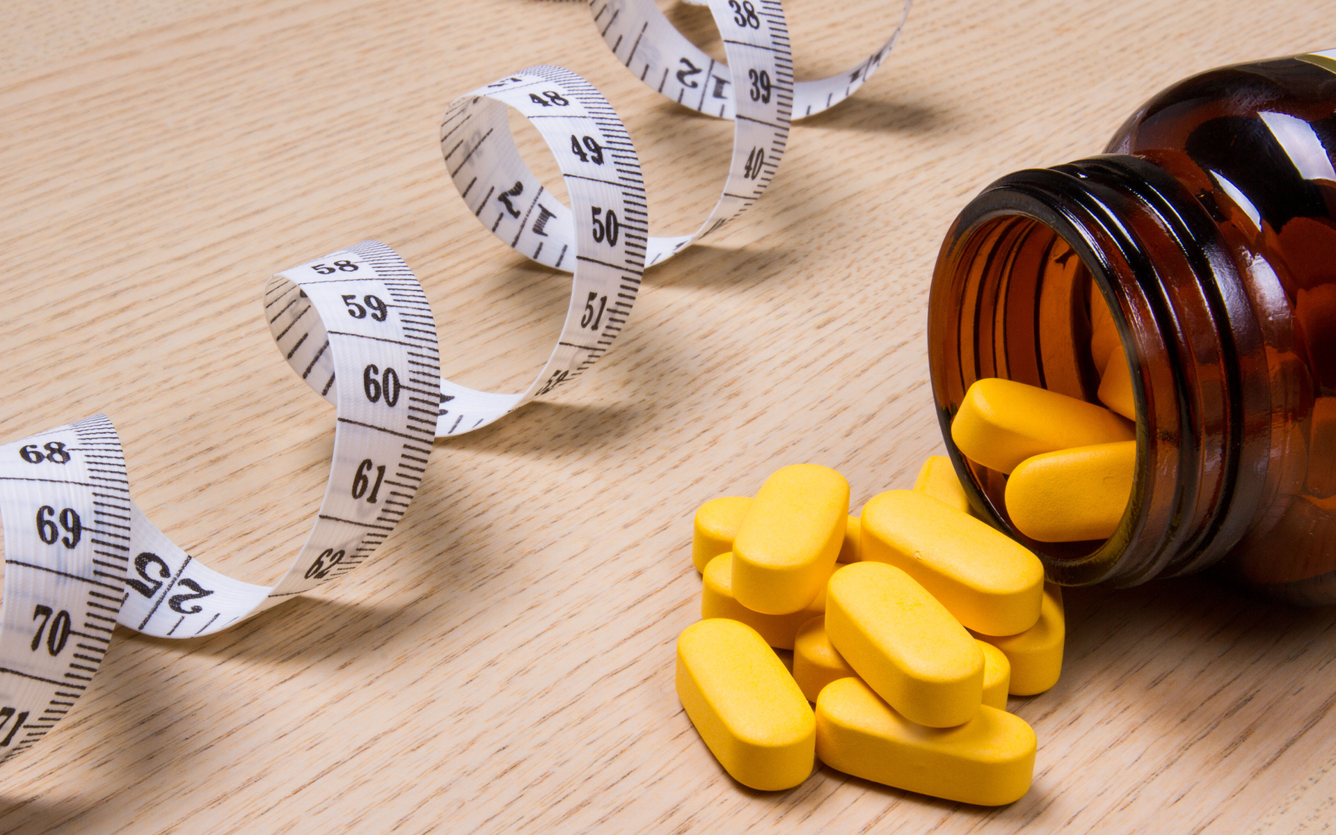 A measuring tape and a bottle of pills on a wooden table.