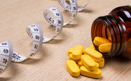 A measuring tape and a bottle of pills on a wooden table.