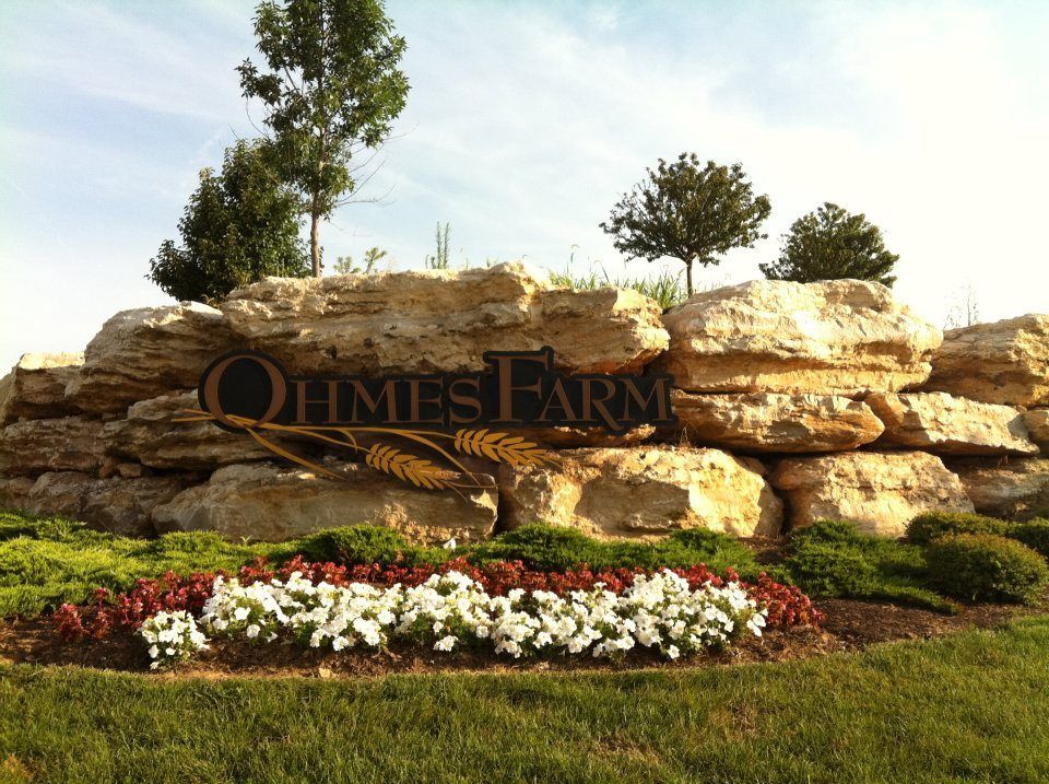 A sign for himes farms is surrounded by rocks and flowers