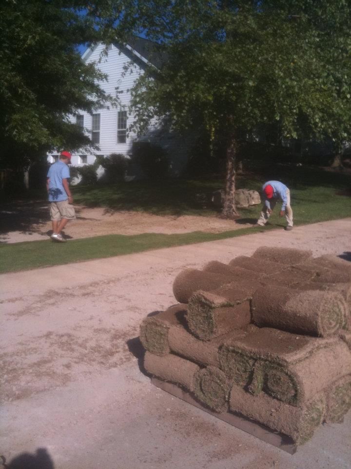 Two men are working on a lawn in front of a white house.