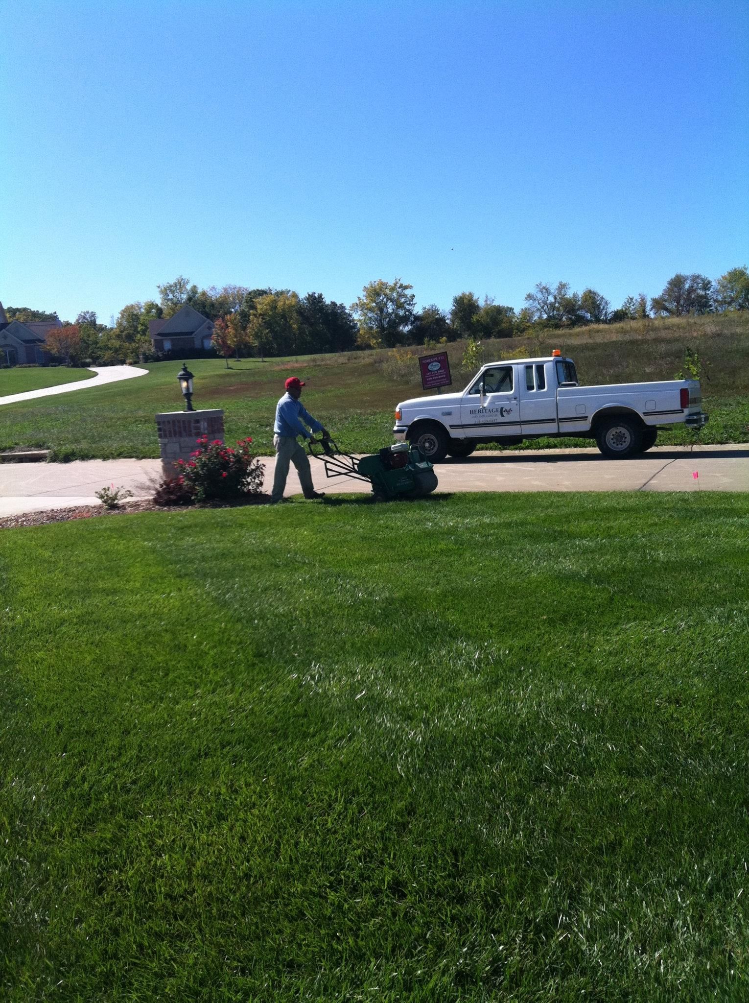 A man is mowing the grass in front of a white truck.