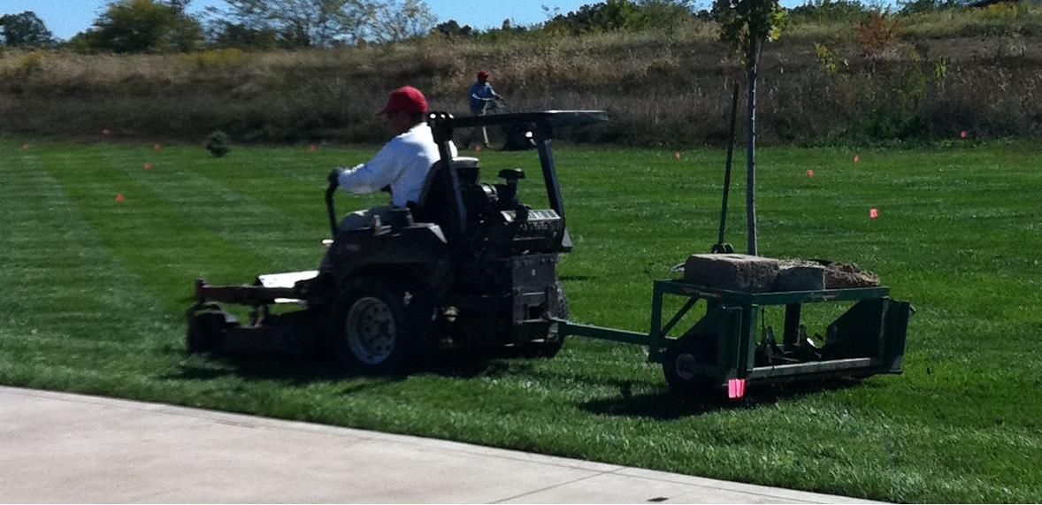 A man is riding a lawn mower on a lush green field.
