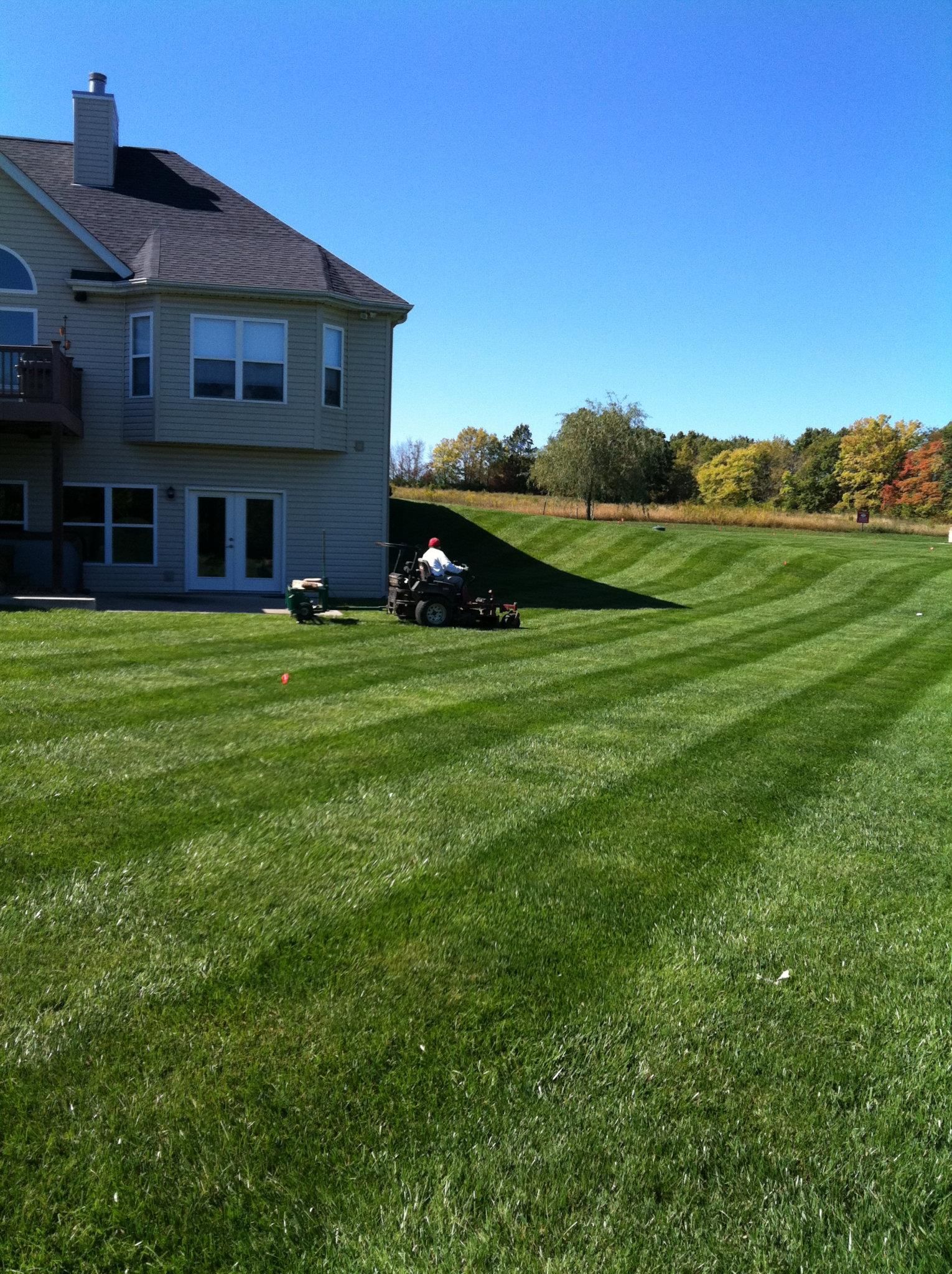 A lawn mower is cutting a lush green lawn in front of a house.