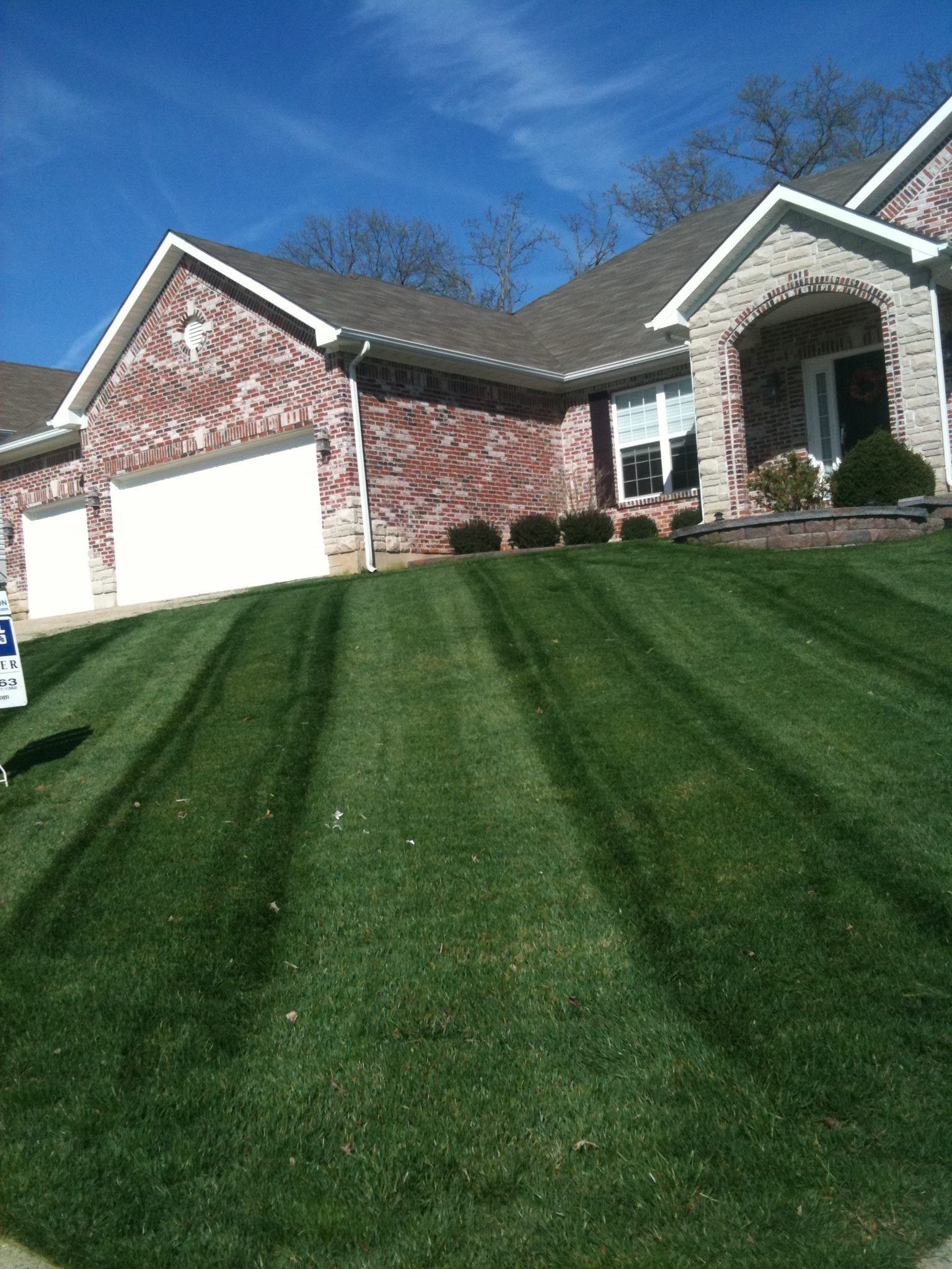 A house with a lush green lawn and a for sale sign in front of it.