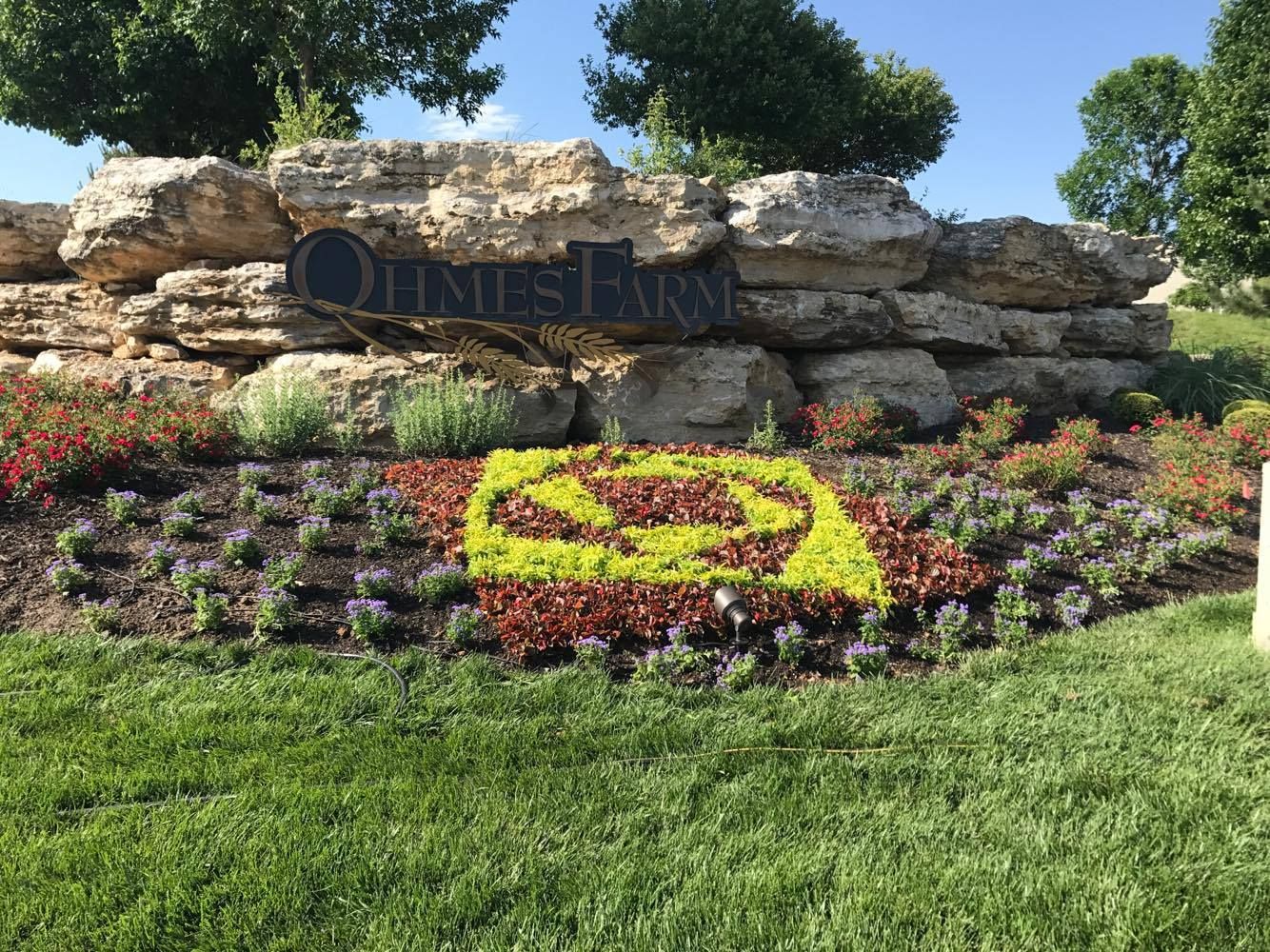 A sign for quinnes farm is surrounded by flowers and rocks