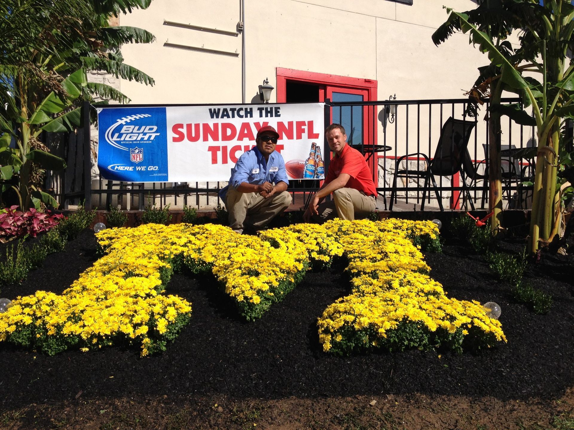 Two men sit in front of a sign that says watch the sunday nfl ticket