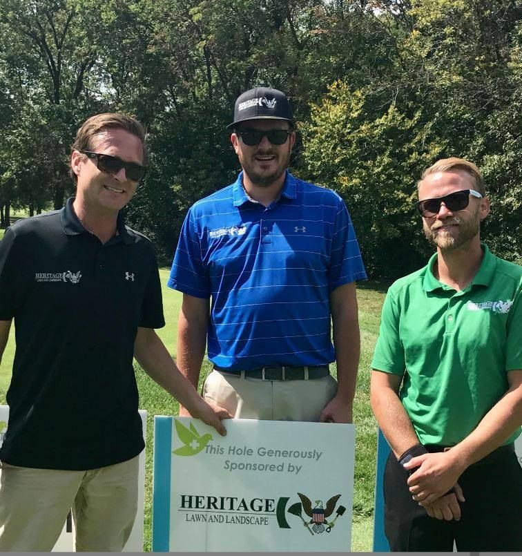 Three men standing next to a sign that says heritage