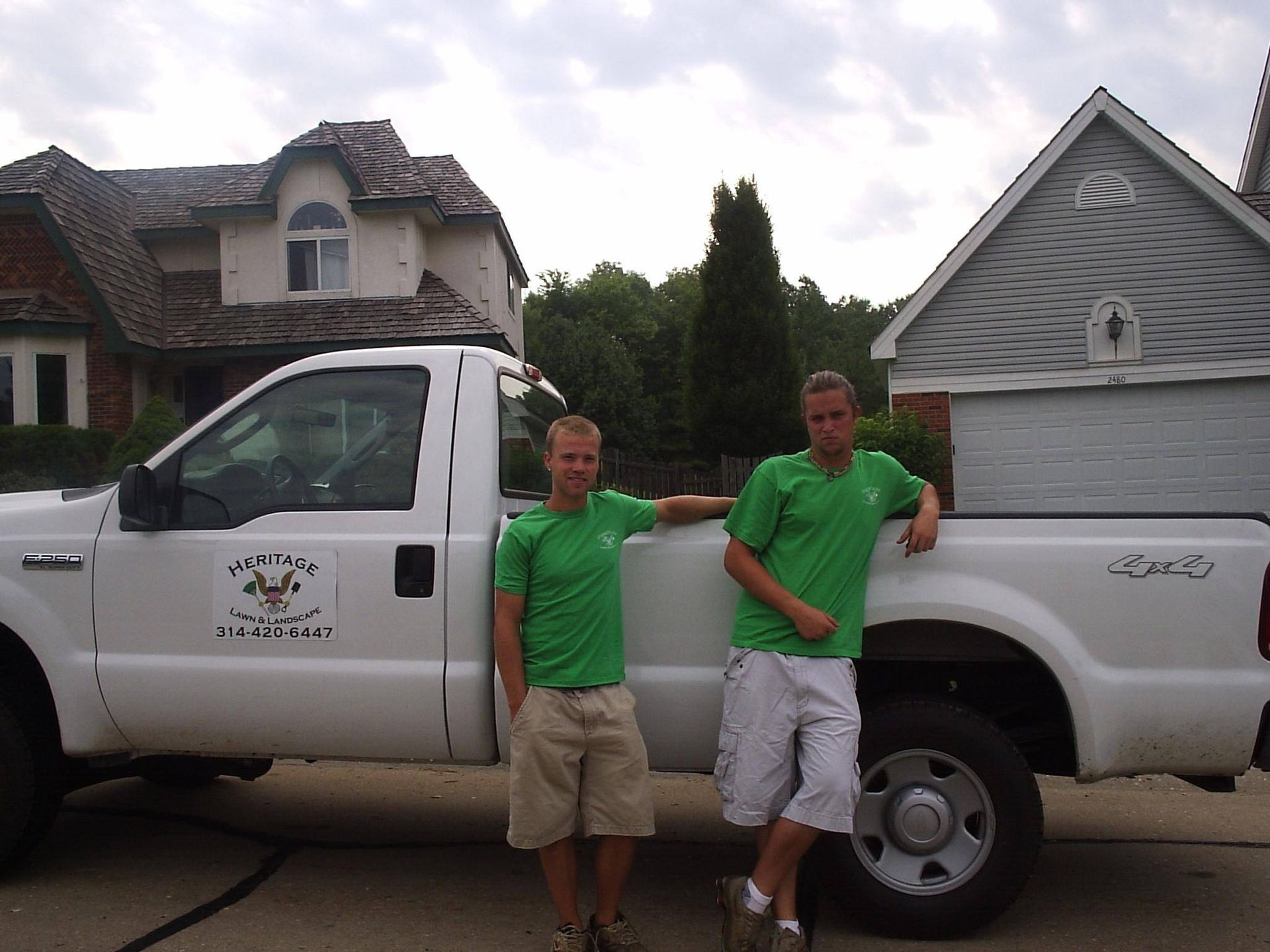 Two men in green shirts are standing next to a white truck