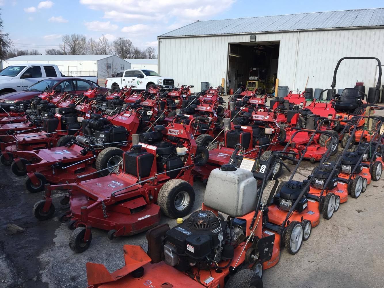 A lot of lawn mowers are parked in front of a building.