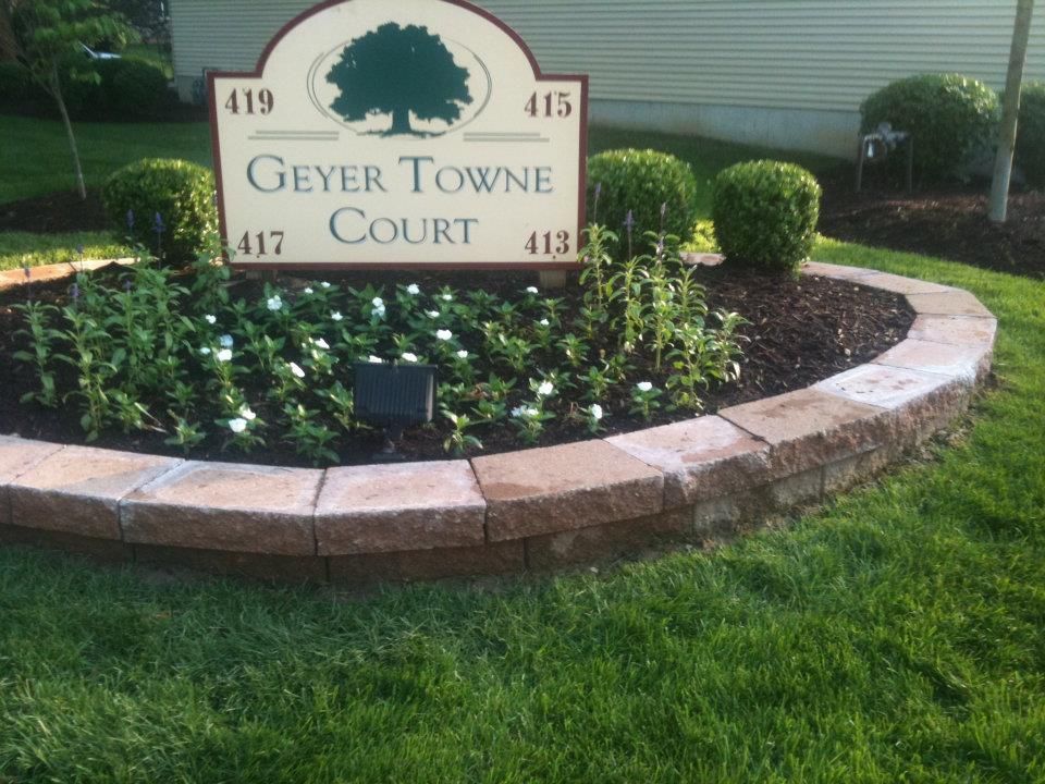 A sign for geyser towne court is surrounded by flowers
