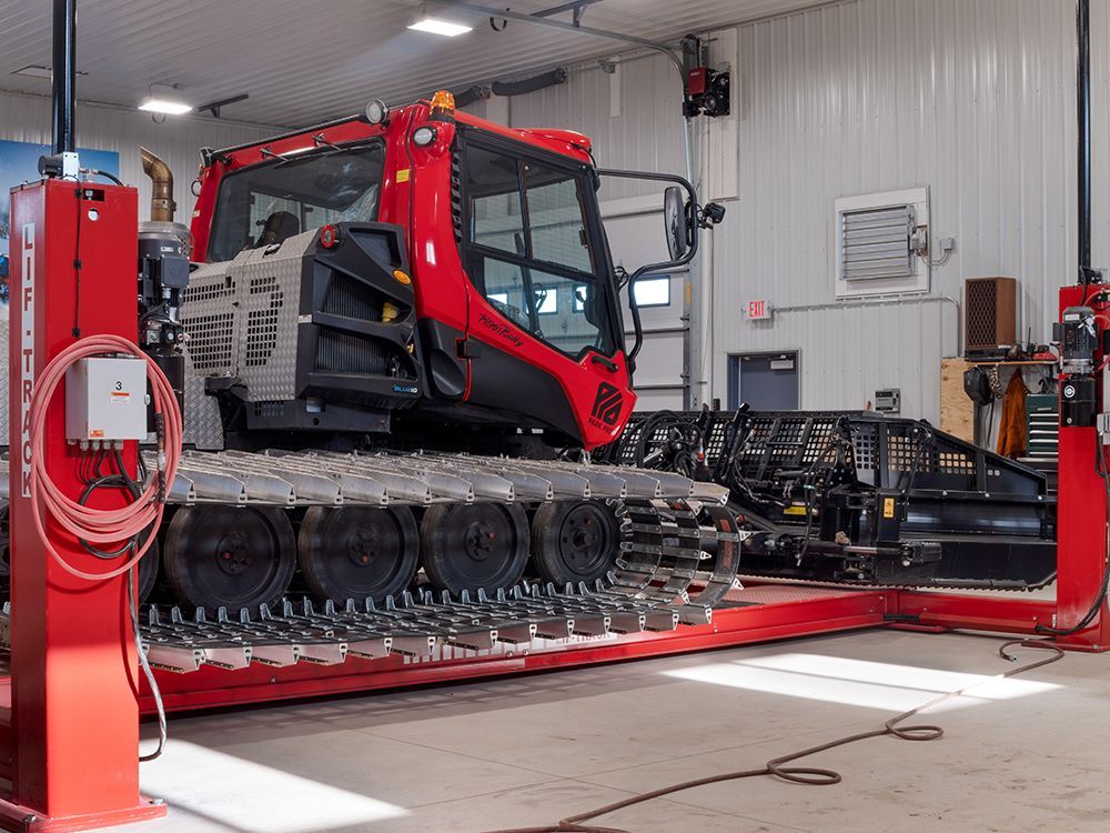 A snow plow is sitting on a red lift in a garage.