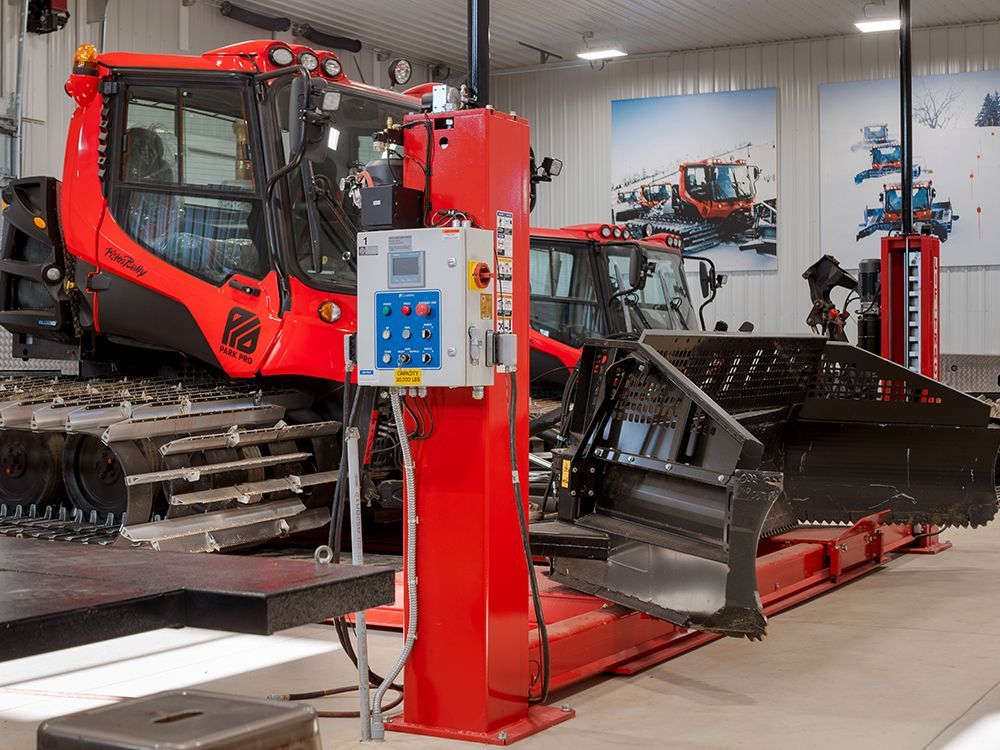 A snow plow is sitting on a lift in a garage.