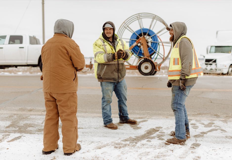 A group of men are standing in the snow talking to each other.