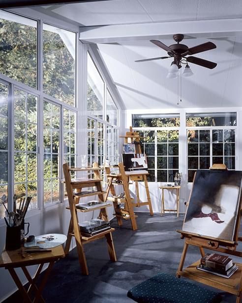 A room with a painting on an easel and a ceiling fan