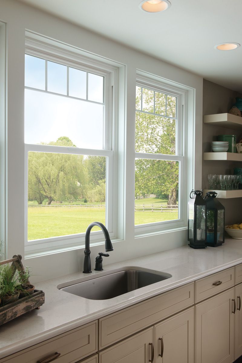 A kitchen with a sink and two windows with a view of a field.