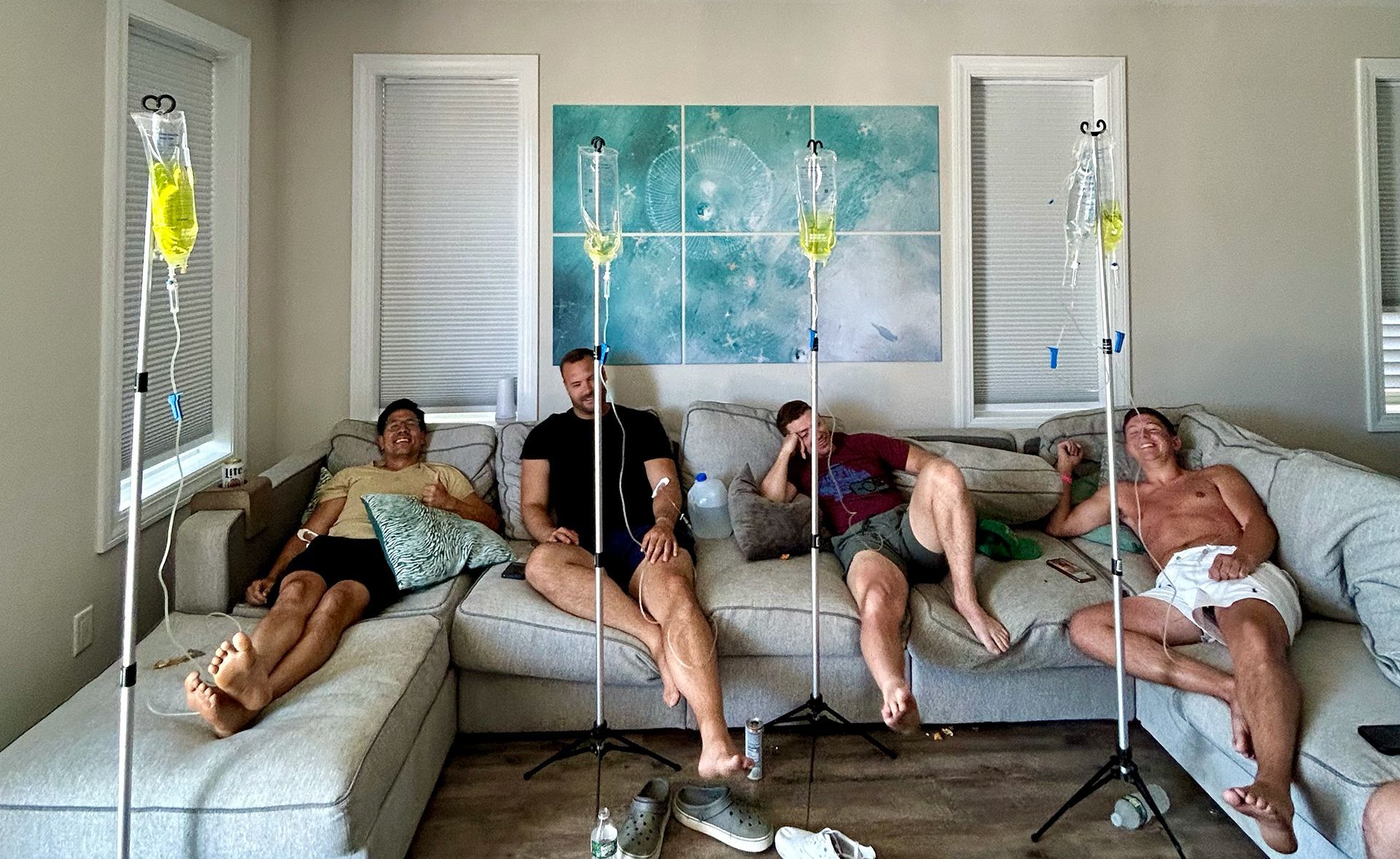 A group of men are sitting on a couch with iv drips in their mouths.