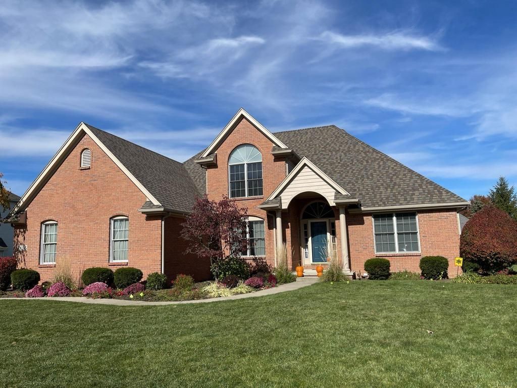 Red brick house with a green lawn and autumn landscaping under a blue sky.