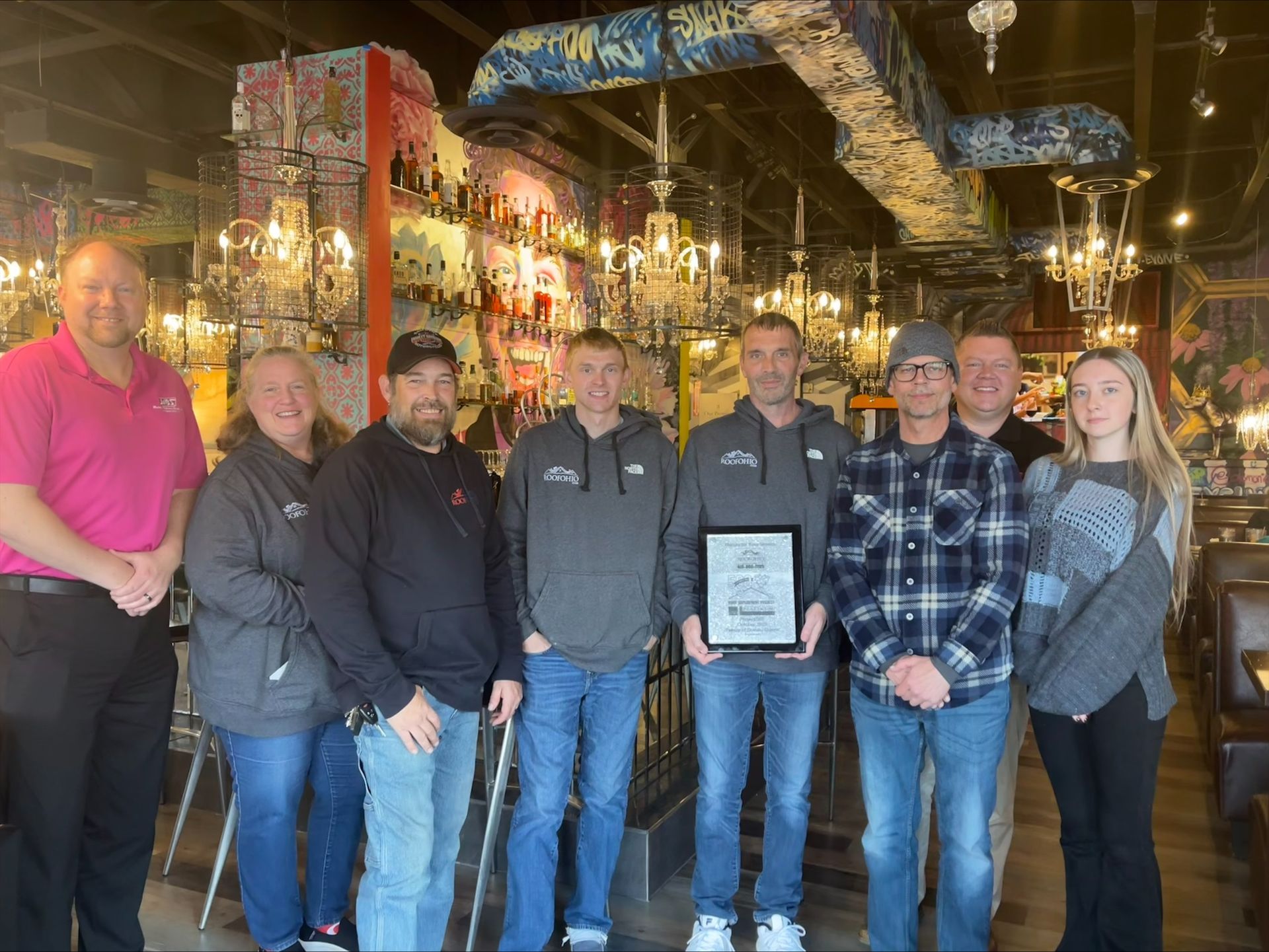 Group of people holding a framed award in a restaurant with colorful decor.