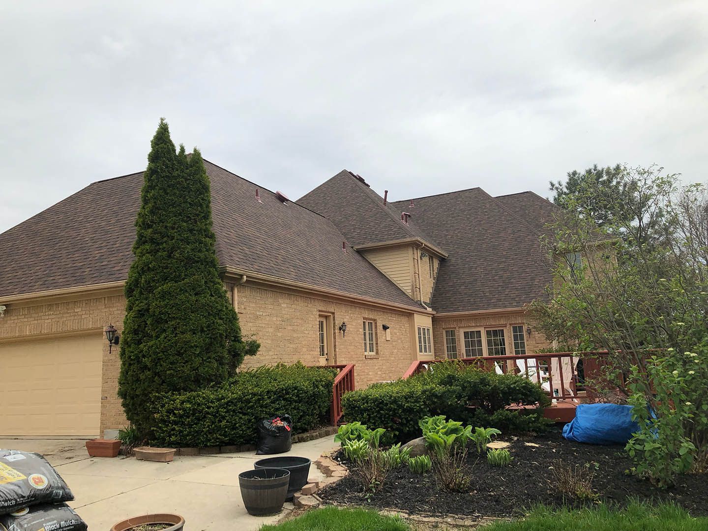 Brick house with brown roof, attached garage, and landscaping in front.