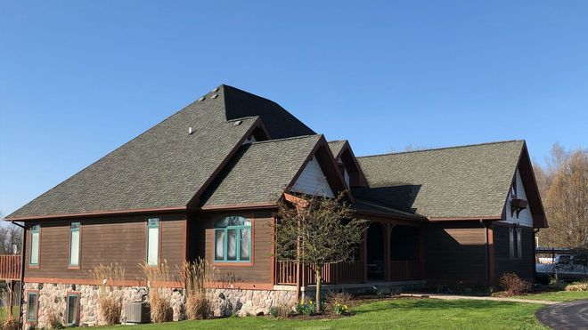 Brown house with multiple roof sections against a blue sky, featuring stone and wood exterior details.