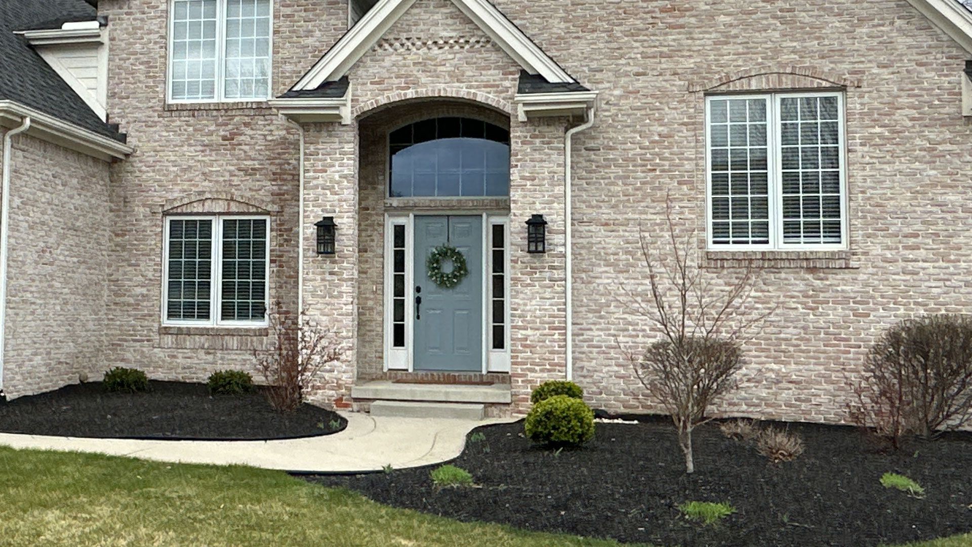 A brick house with a blue door and black mulch landscaping.