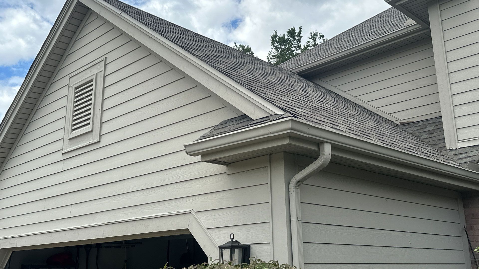 Beige house exterior with a gray shingled roof, white trim, and a window vent.
