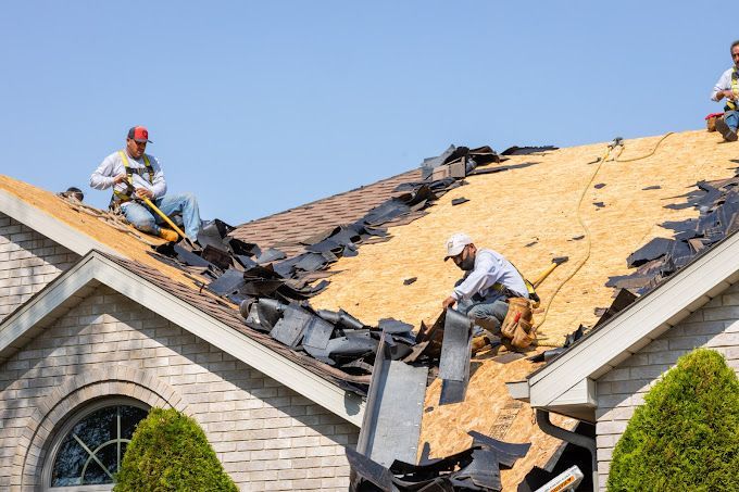 Roofers removing old shingles from a house roof on a sunny day.