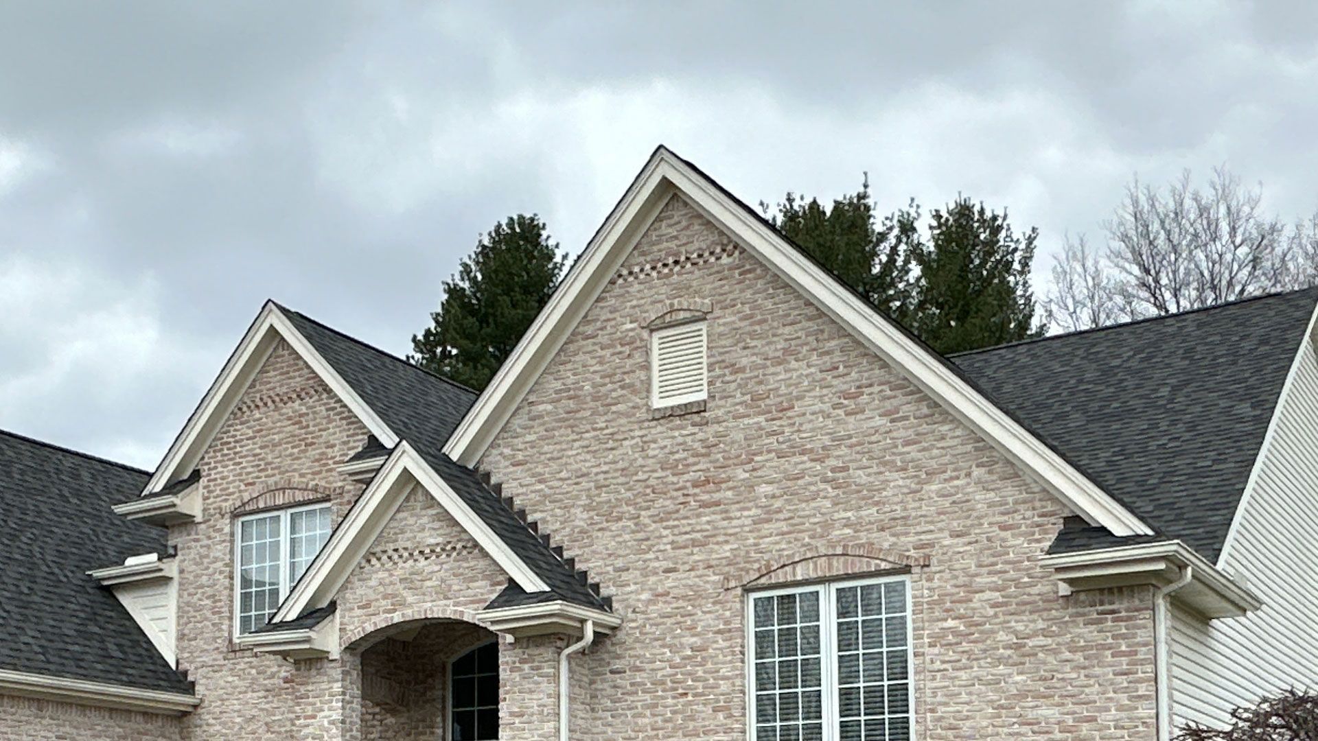 Brick house with dark roof and white trim under cloudy sky.
