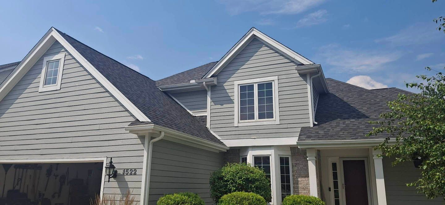 Gray house with dark gray roof against a blue sky, trimmed in white.