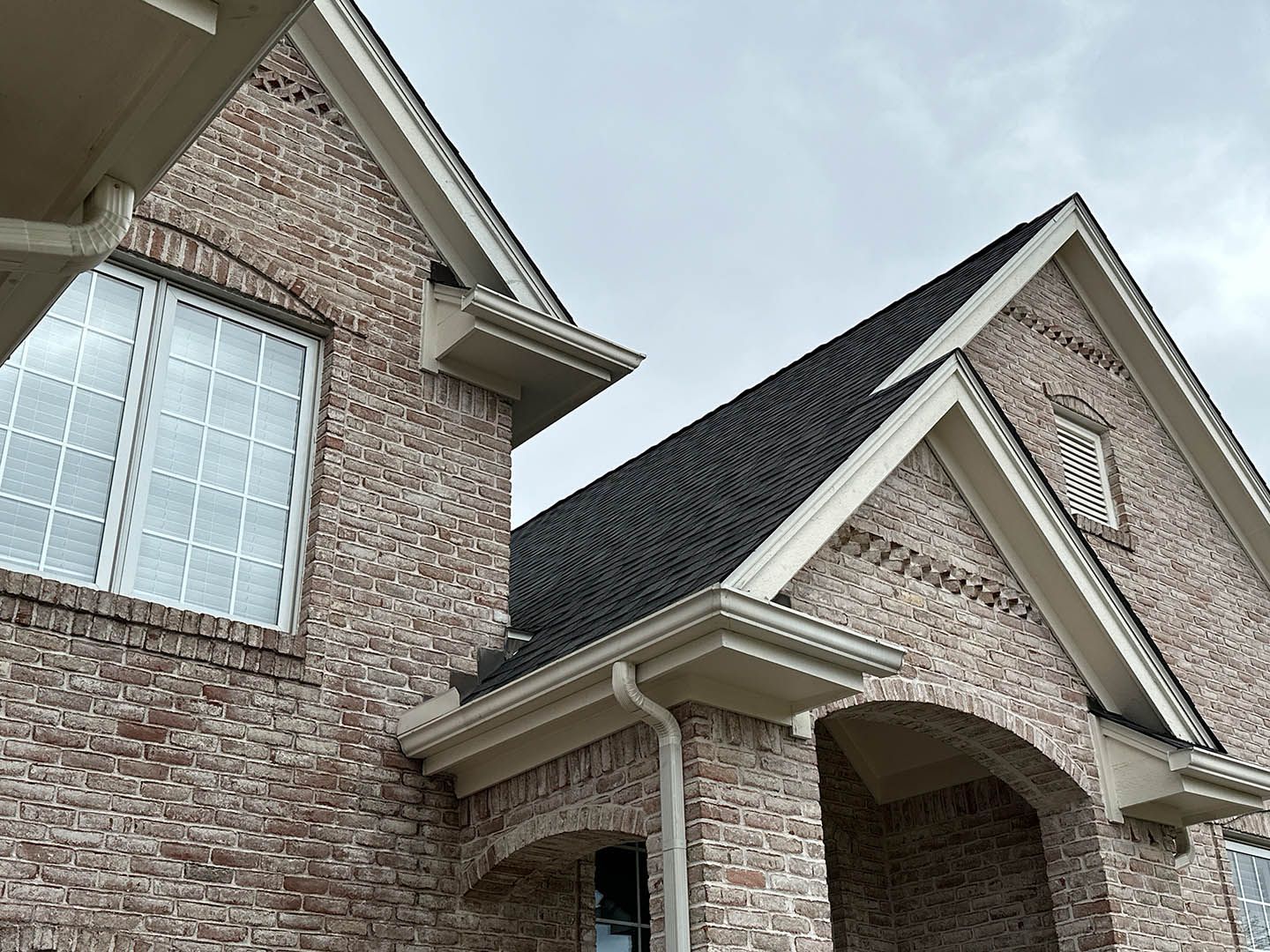 Brick house exterior with dark shingle roof, white trim, and a cloudy sky.