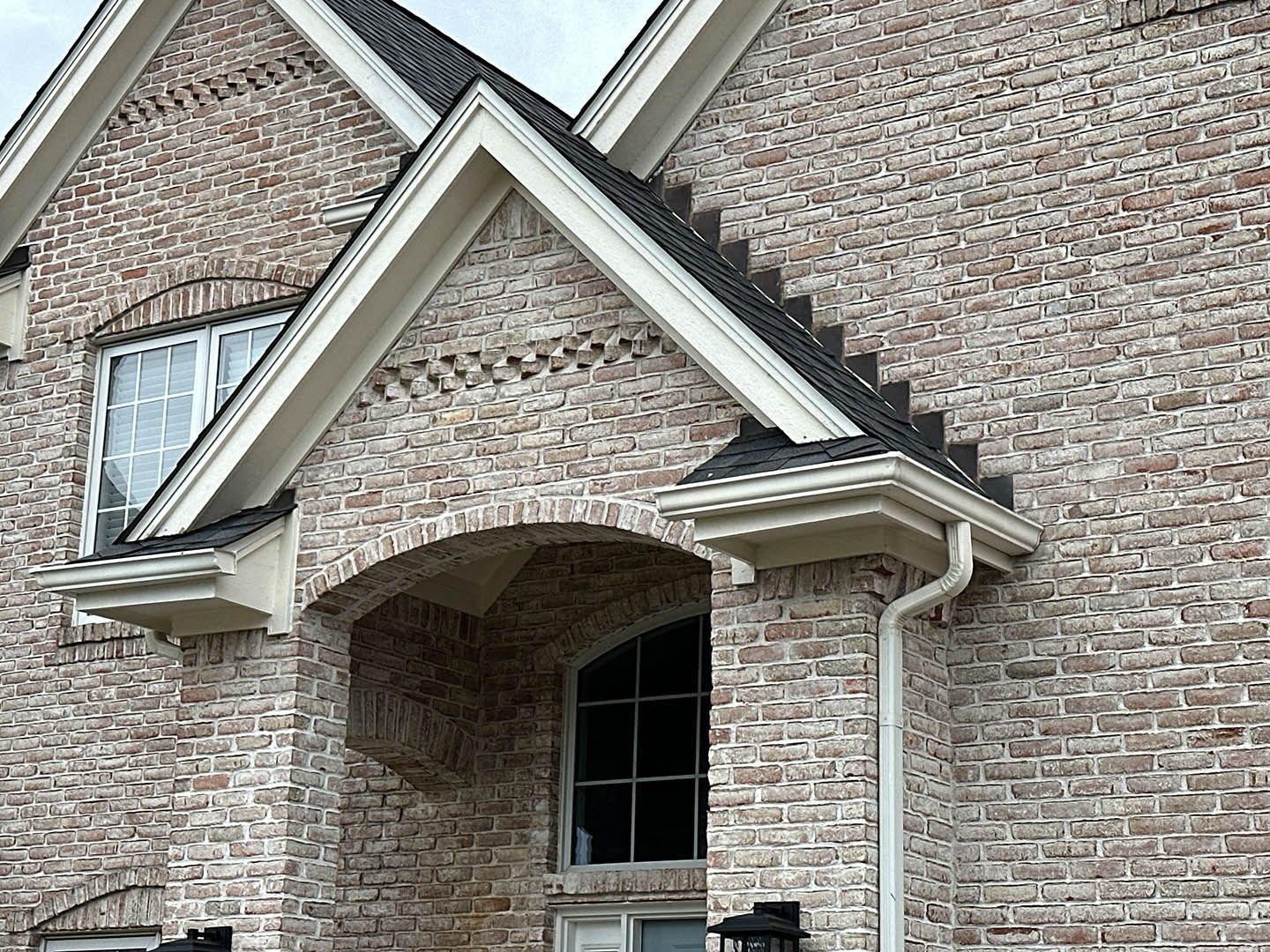 Brick exterior of a house with arched entryway, white trim, and a dark roof.