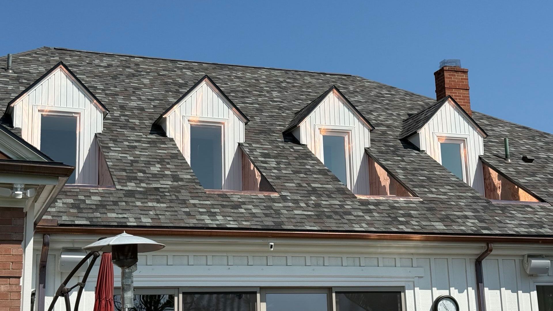 White house with four dormers and a gray shingle roof under a clear, blue sky.